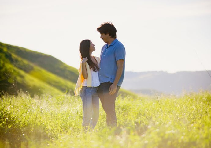 A young Mexican couple smile as they spend time with one another in a fresh grass field on the outskirts of Los Angeles, California, USA.  Young love.